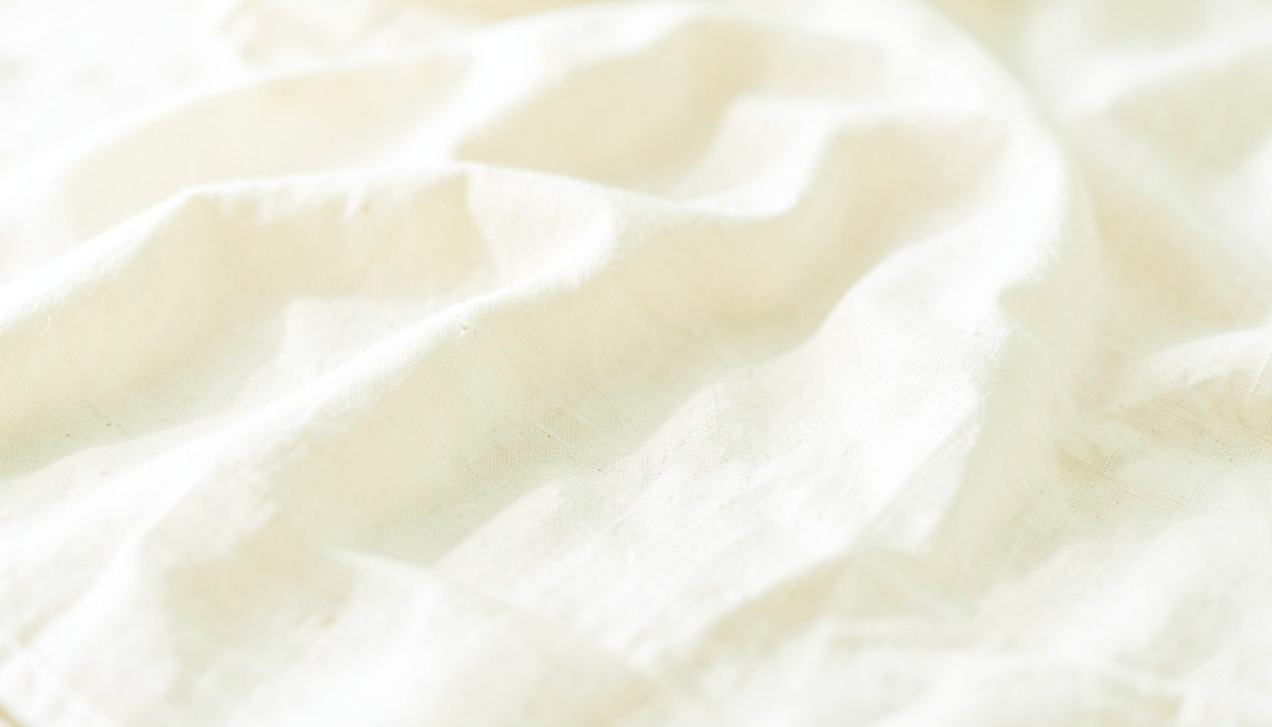 Bright airy high-key photograph of pale linen fabric softly draped across a sunlit surface, warm white and sand tones, calm and neutral atmosphere.